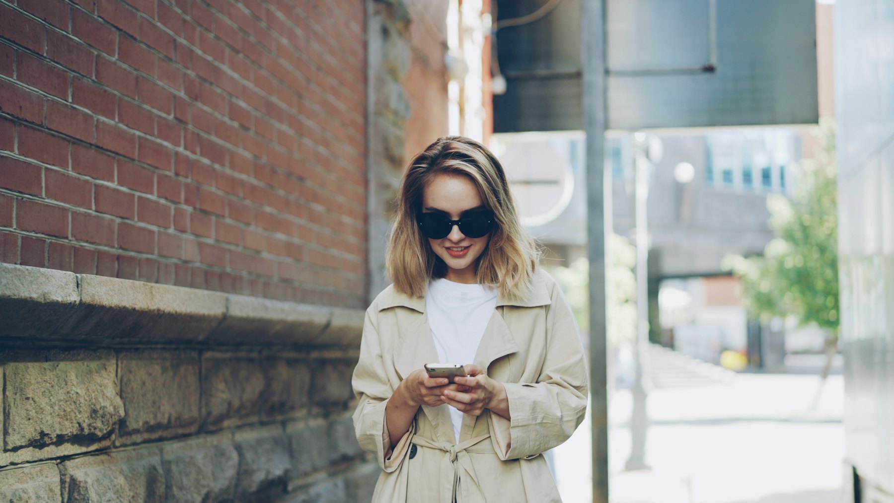 A woman in a trench coat checking her phone on the street