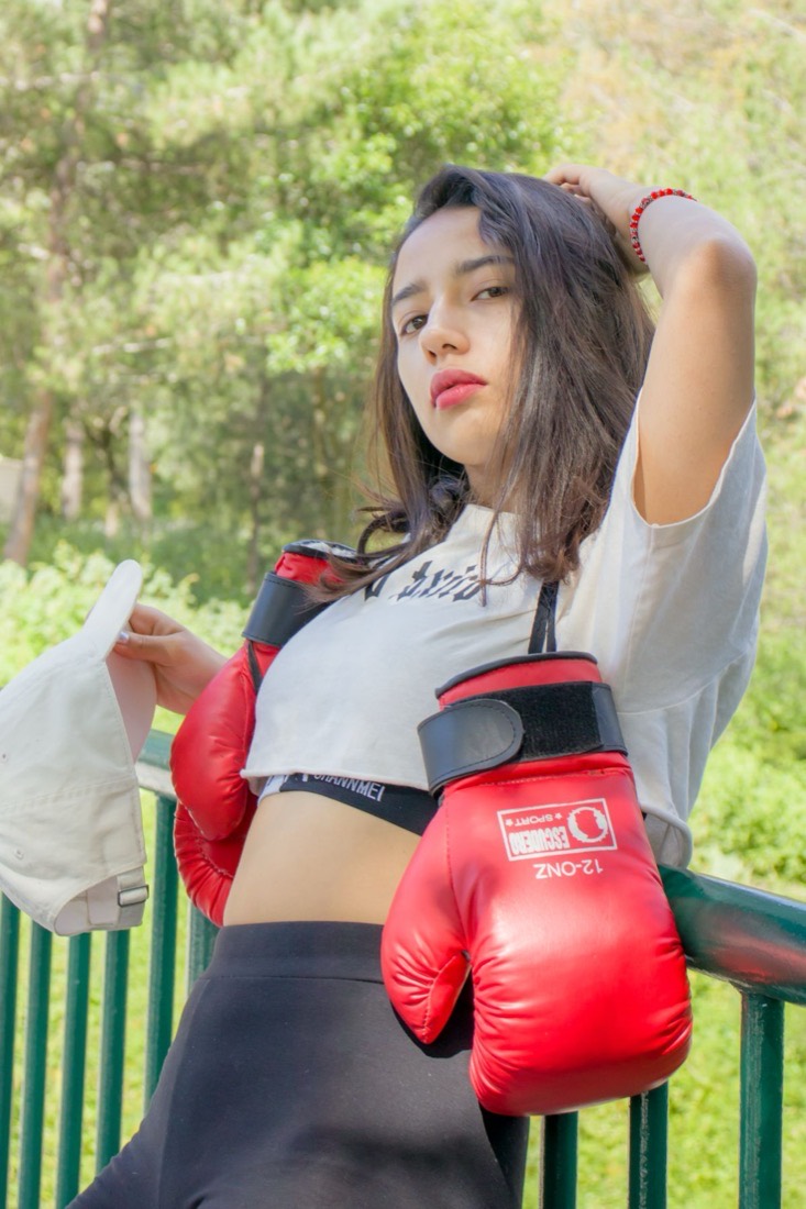 A woman in red boxing gloves leaning against a railing outdoors