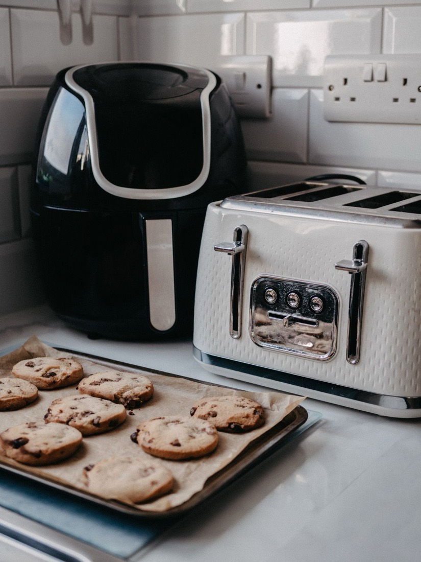 A black air fryer and a white toaster on a kitchen counter beside a tray of fresh cookies