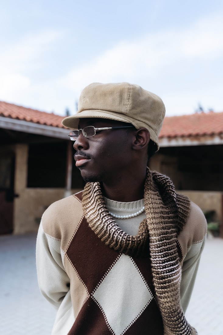 A man in a brown and cream argyle knit with a fringed scarf
