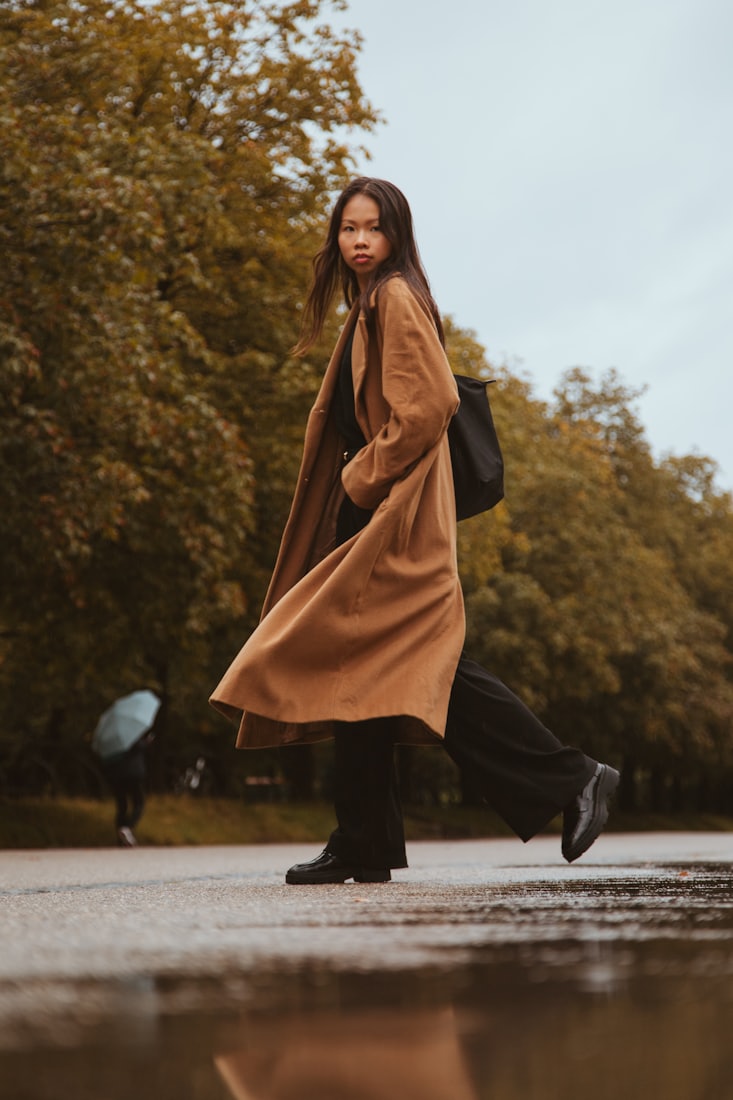 A woman crossing a park in a long camel coat