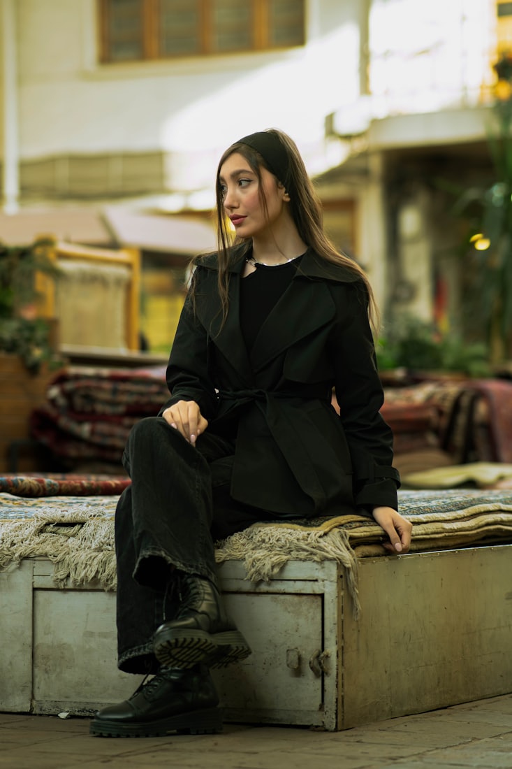 A woman in a dark trench sitting outside a rug shop